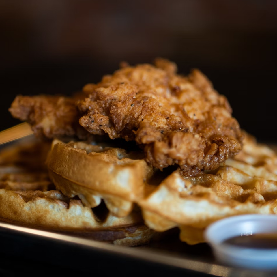 Crispy fried chicken pieces piled on golden waffles with a side of syrup at Brenda's Sports Bar & Grill.