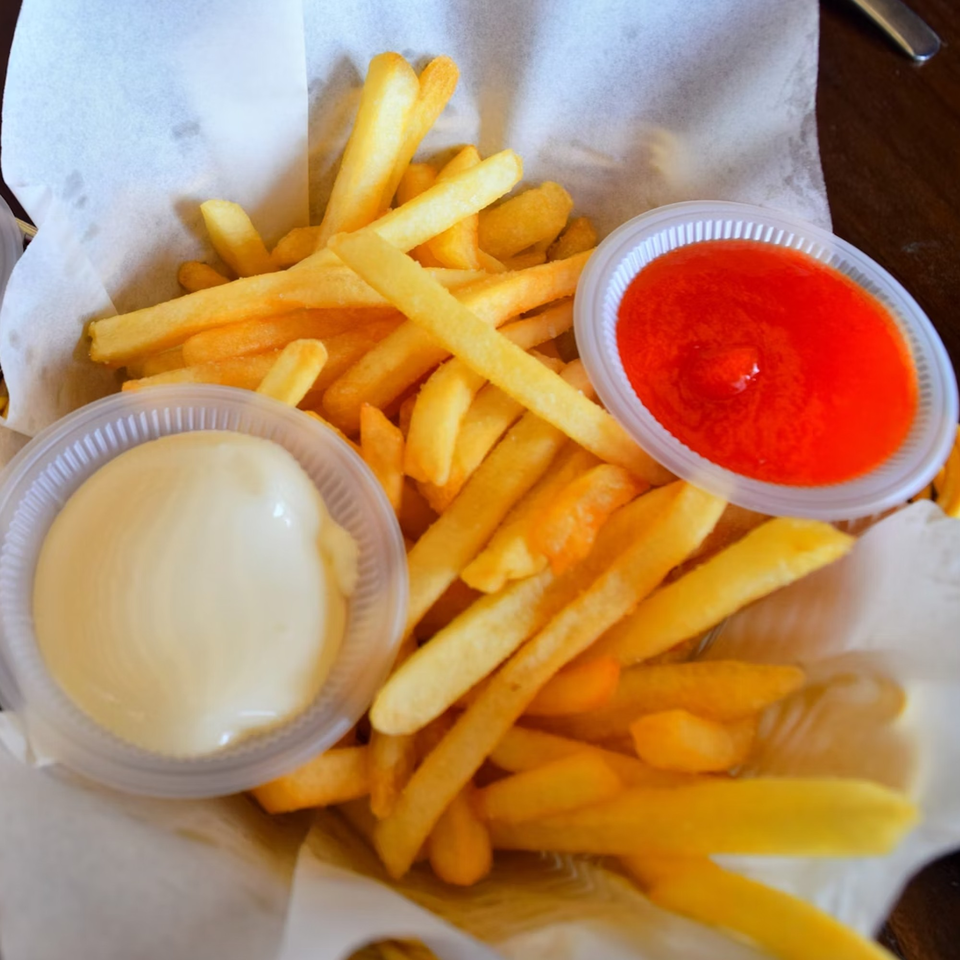 Golden french fries in a paper-lined basket with small cups of ketchup and mayonnaise.