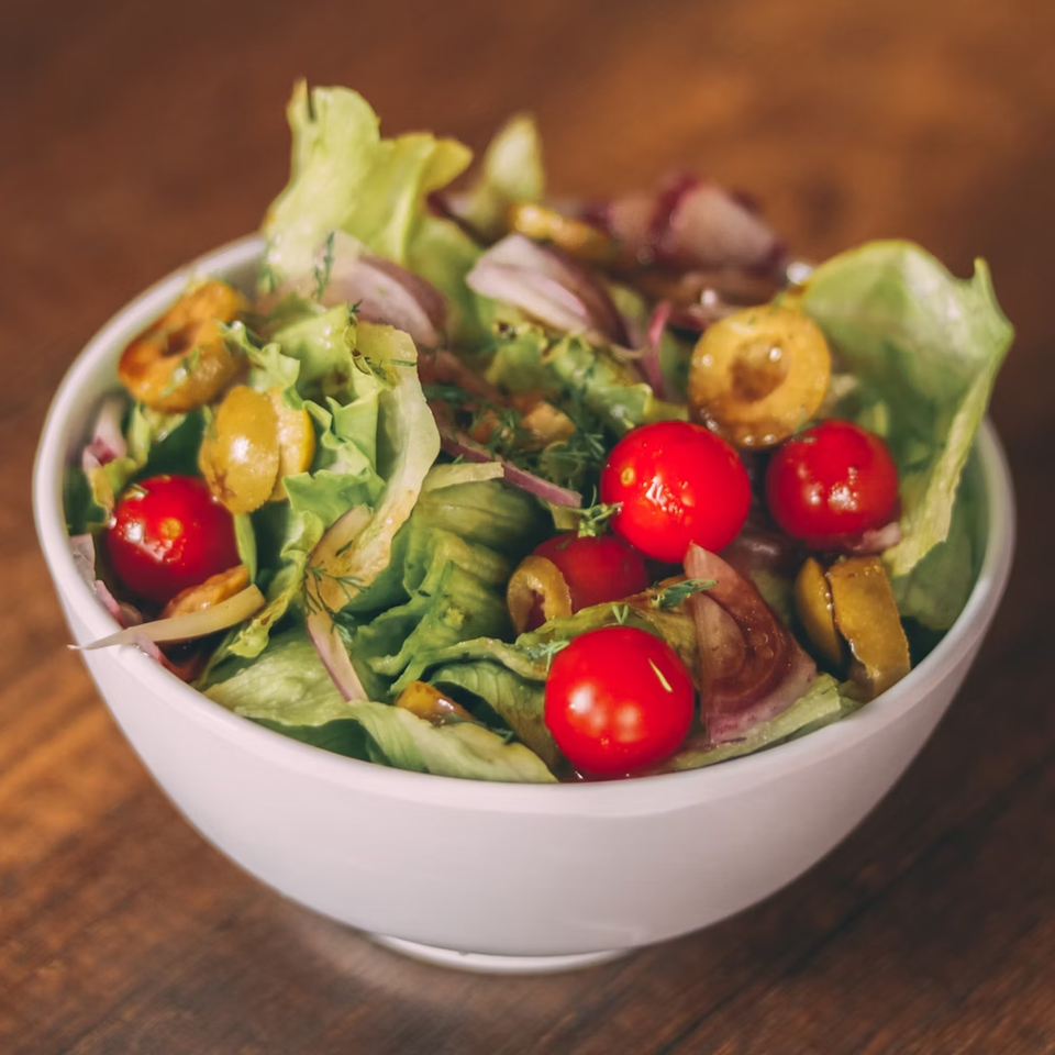 Fresh green salad with cherry tomatoes, olives, and red onion in a white bowl.