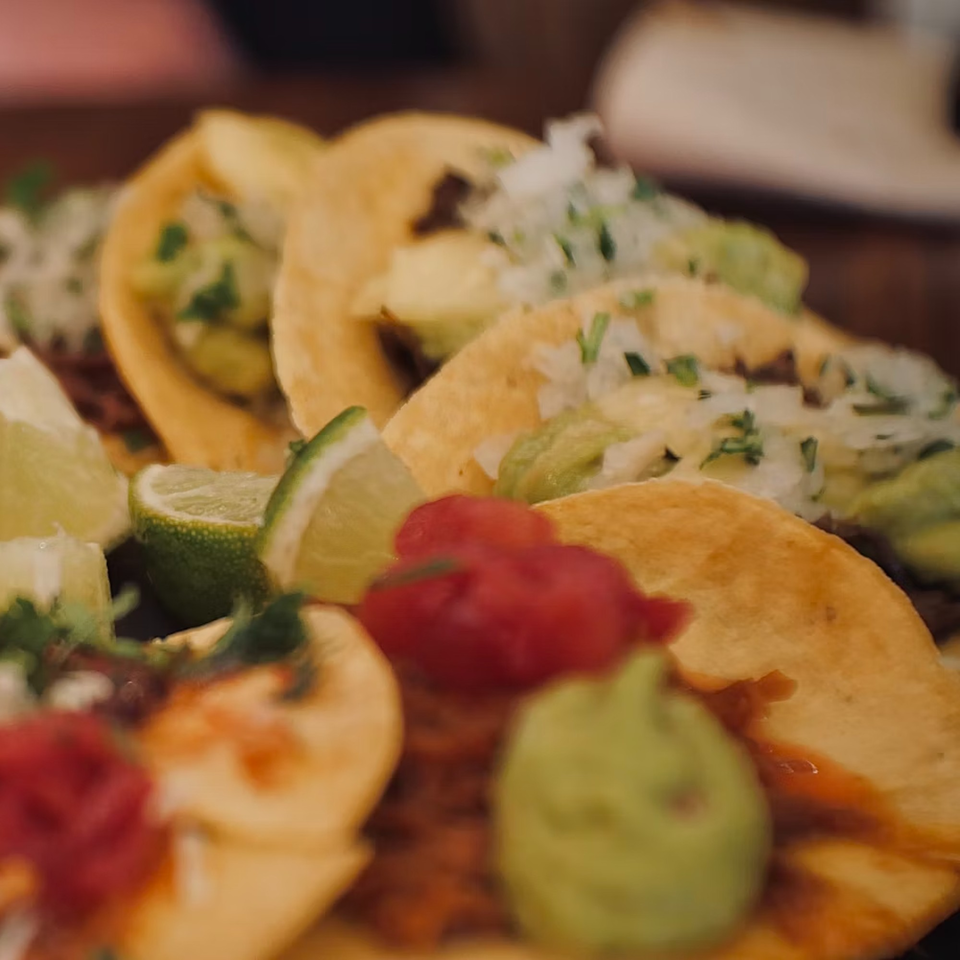 Close-up of several tacos with various toppings, including guacamole, diced onions, and lime wedges.