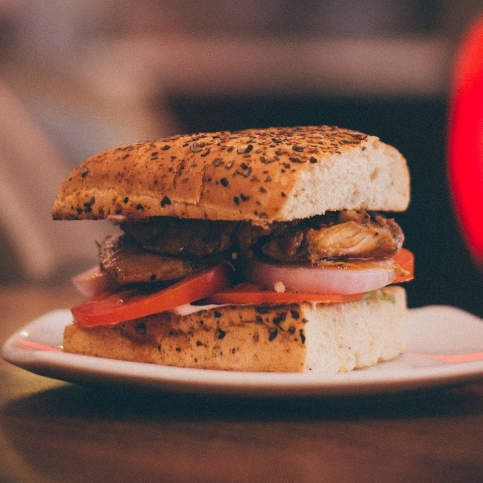 Close-up of a chicken sandwich with tomatoes and onions on a seeded bun from Brenda's Sports Bar & Grill.
