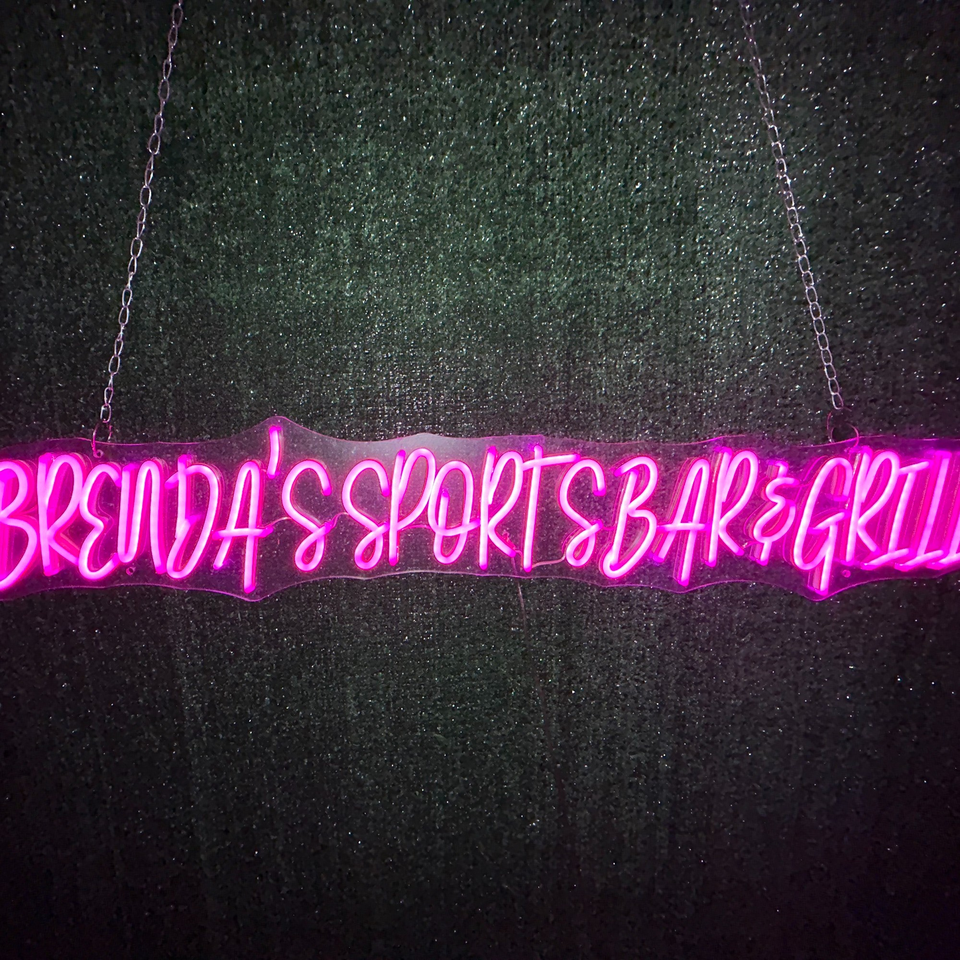 Pink neon sign for Brenda's Sports Bar & Grill hanging against a dark, textured background.