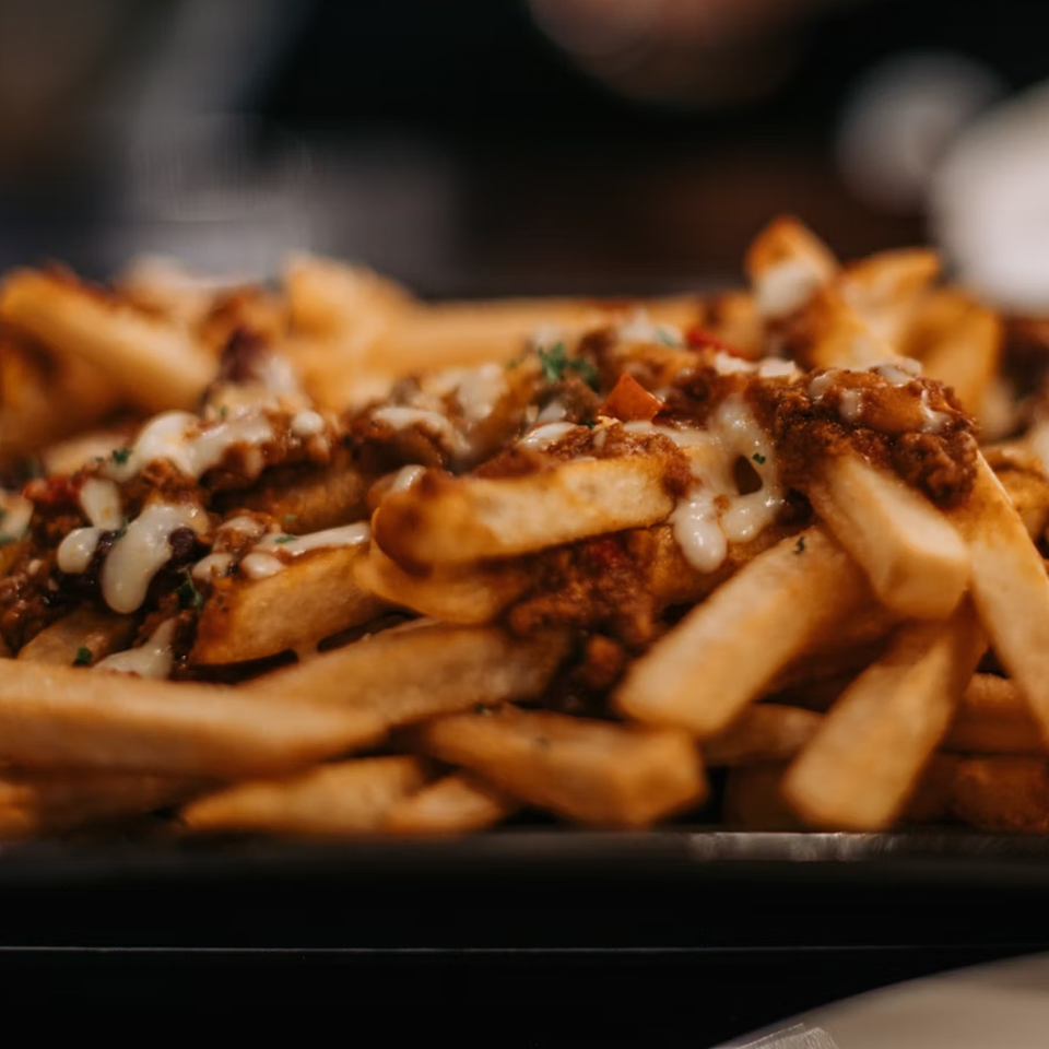 Close-up of golden french fries topped with chili, melted cheese, and herbs at Brenda's Sports Bar & Grill.