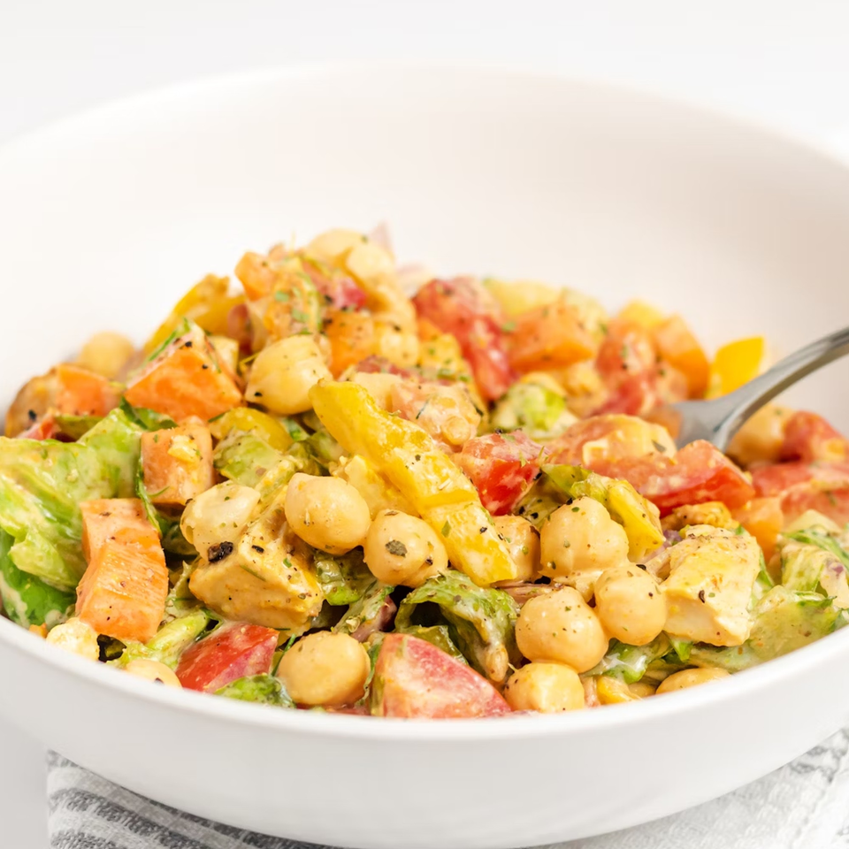 Close-up of a vibrant salad with chickpeas, chicken, tomatoes, and lettuce in a white bowl.