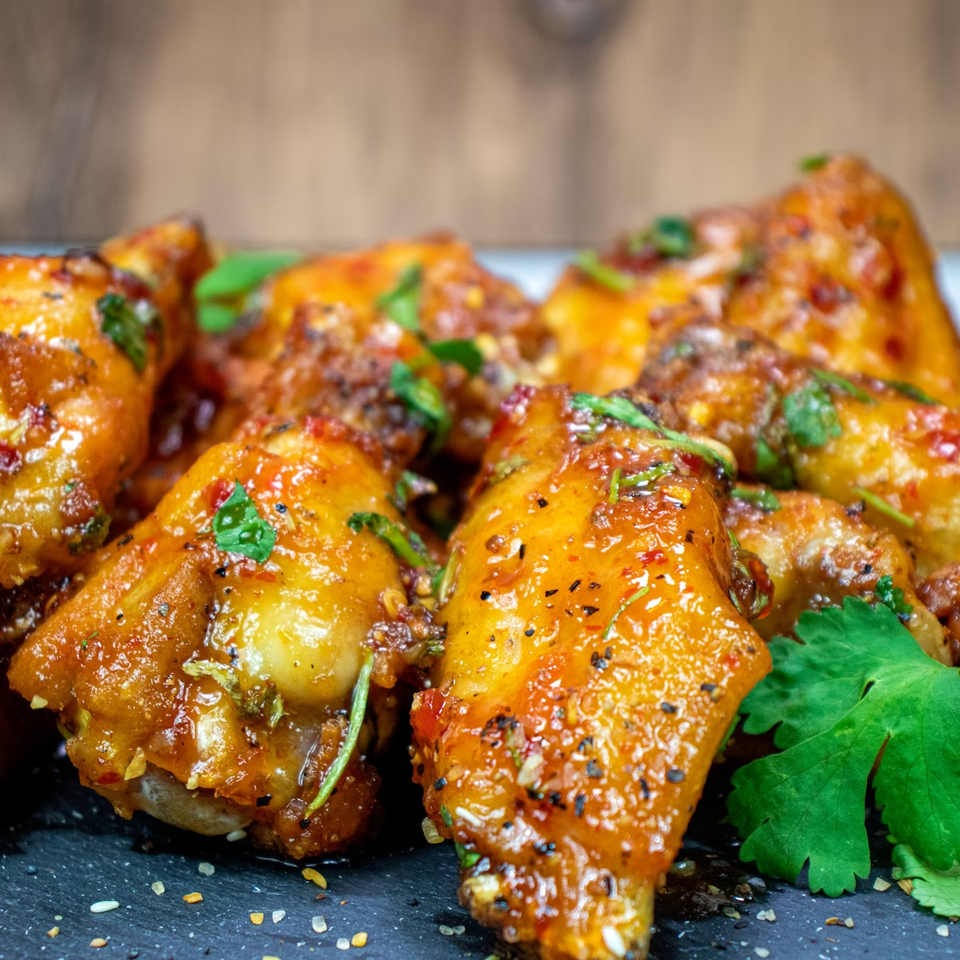 Close-up of several glazed chicken wings garnished with herbs on a dark plate.