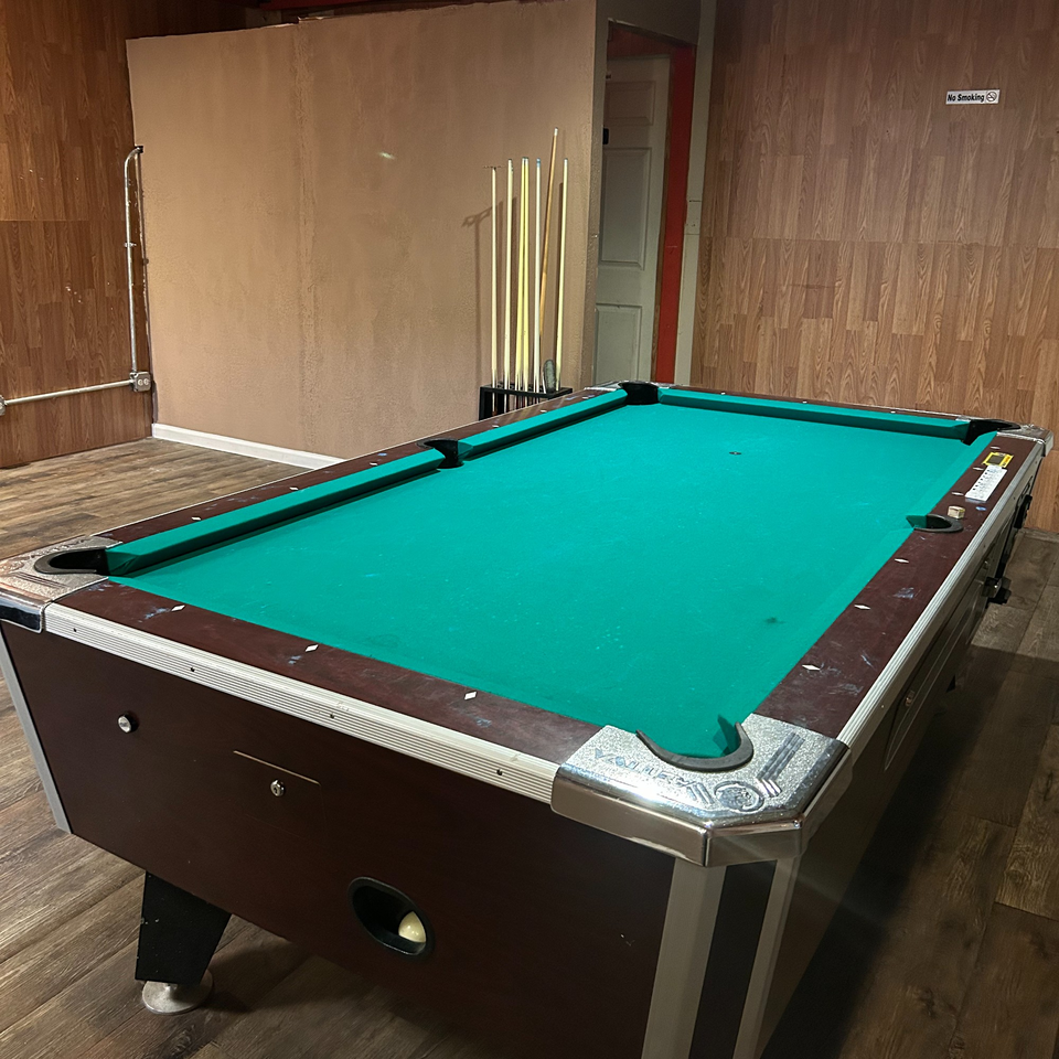 A green-felt pool table with cues in a rack, ready for play at Brenda's Sports Bar & Grill.