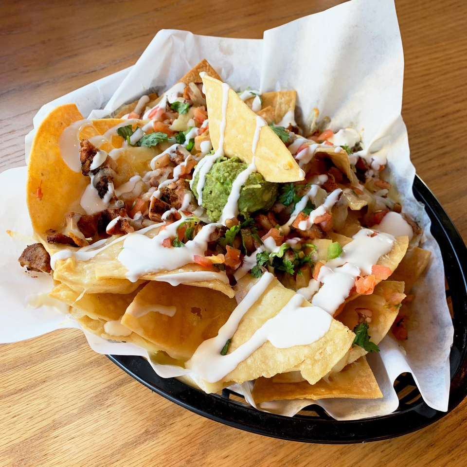 Loaded nachos with chicken, cheese, guacamole, salsa, and sour cream in a basket.
