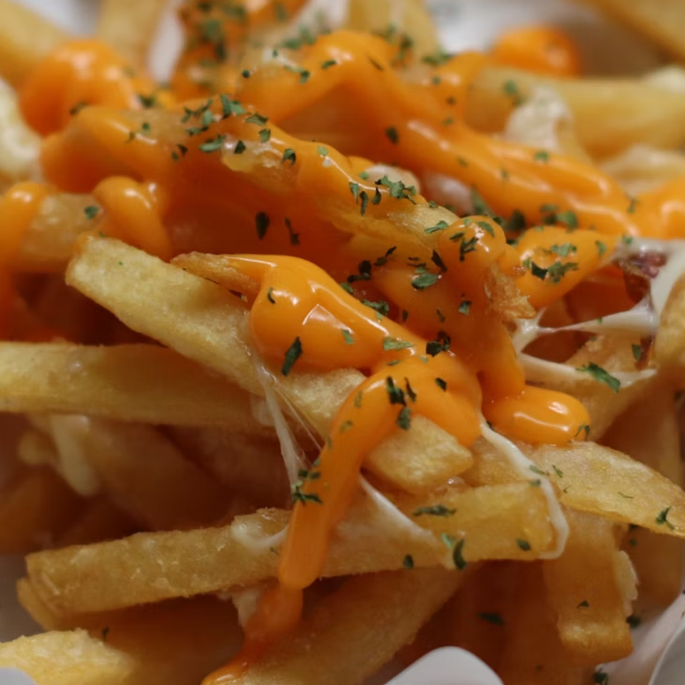 Close-up of golden french fries generously topped with melted cheese sauce and green herbs.