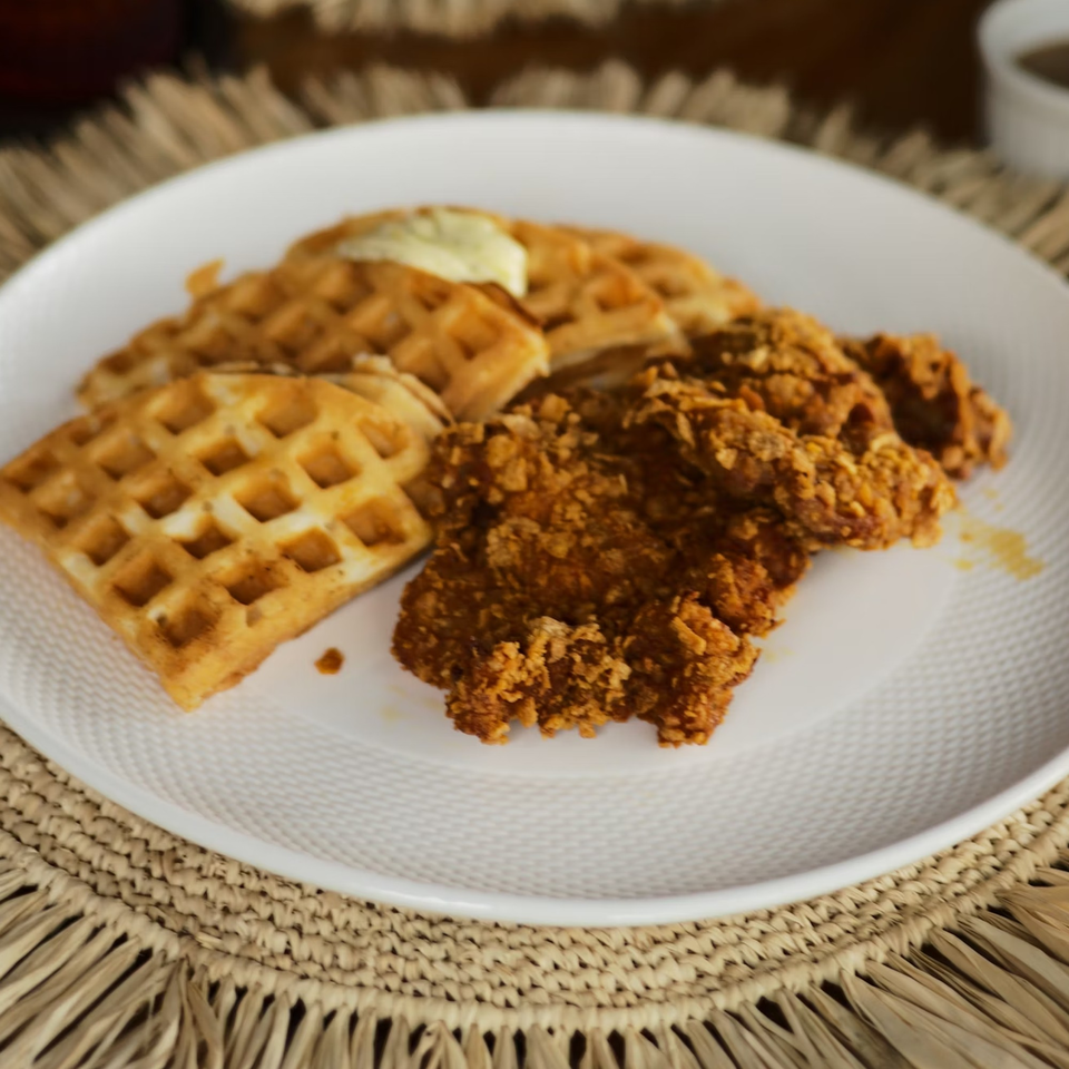 Crispy fried chicken and waffles with butter on a white plate at Brenda's Sports Bar & Grill.