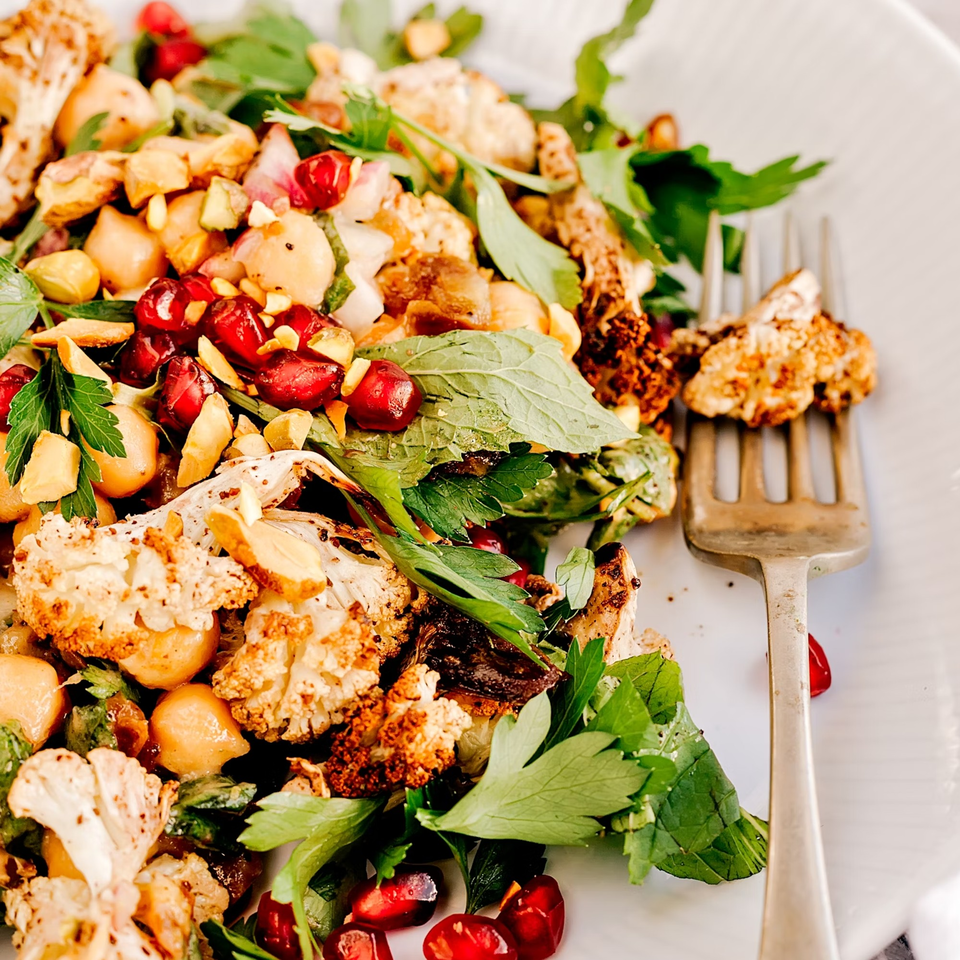 Roasted cauliflower and chickpeas with pomegranate seeds, herbs, and nuts on a white plate.